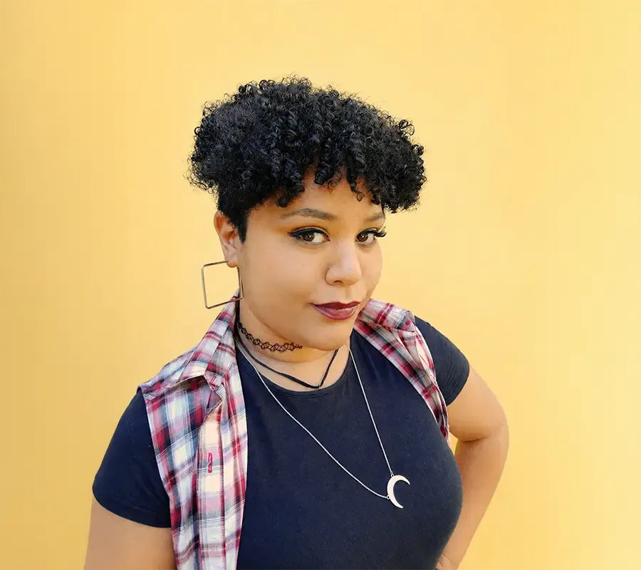 Carmen Williams, a copywriter with short curly hair, smiling in front of a yellow wall