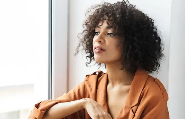 A woman with natural curly hair sitting by a window
