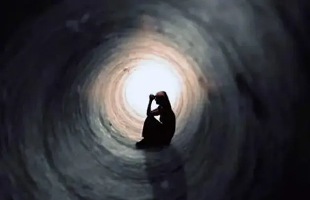 A lone figure sitting at the bright end of a dark tunnel