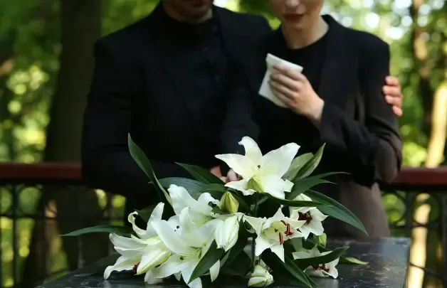 Mourners in black holding white lilies at a funeral