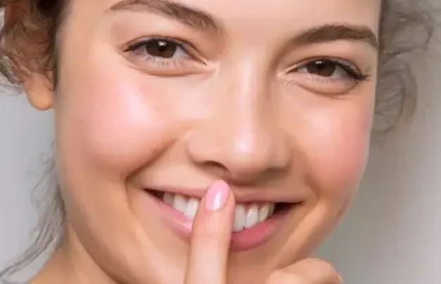A smiling woman with a finger to her lips, showing white teeth